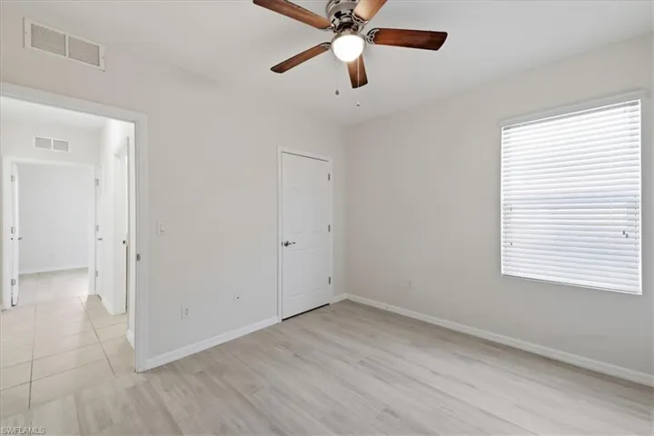 Wood-finish flooring, ceiling fan with integrated lighting, white interior doors, and a window with blinds