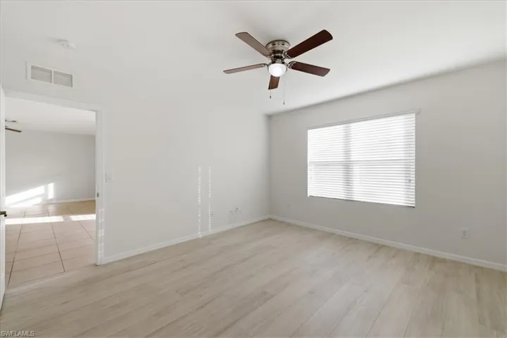 Wood-finish flooring, ceiling fan with integrated lighting, window with horizontal blinds, and white wall finishes