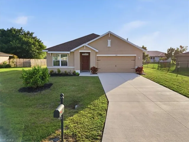 Stucco exterior with an attached garage, a paved driveway, and mature landscaping