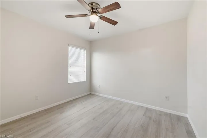 Neutral-toned walls, wood-finish flooring, a window with blinds, and a ceiling fan with integrated lighting