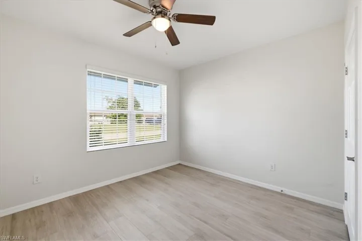 Wood-finish flooring, ceiling fan with integrated lighting, window with blinds, and a white paneled door
