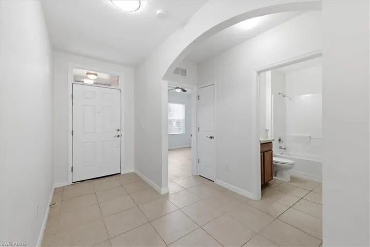 Neutral tile flooring, arched entryway, panel front door with transom window, bathroom with vanity and shower/tub combination