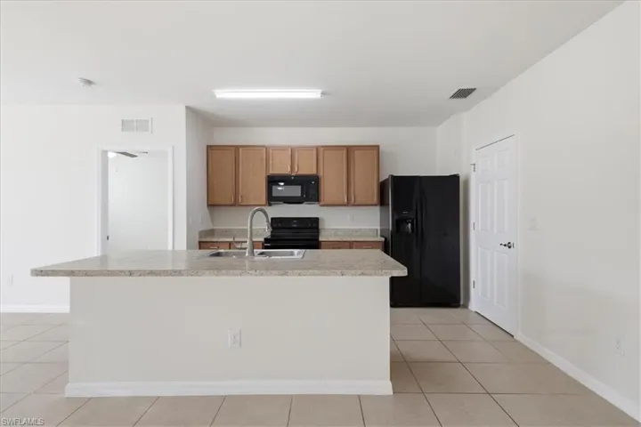 Kitchen featuring a breakfast bar with stone-finish countertop, stainless steel sink with gooseneck faucet, black appliances, and wood-finish cabinetry