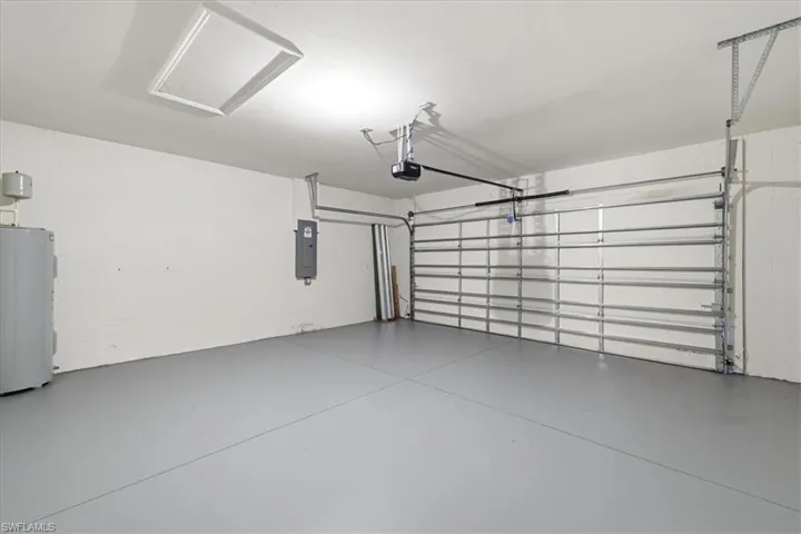 Attached garage with a light grey finished floor, electric garage door opener, and a wall-mounted electrical panel