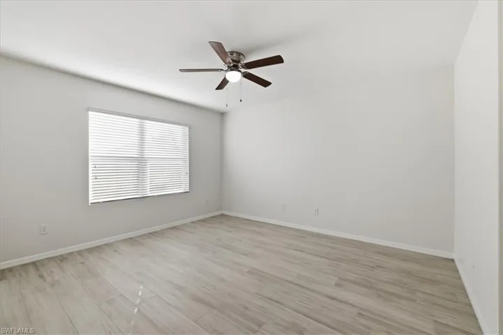 Expansive room featuring wood-finish flooring, a ceiling fan with integrated lighting, and a large window with blinds