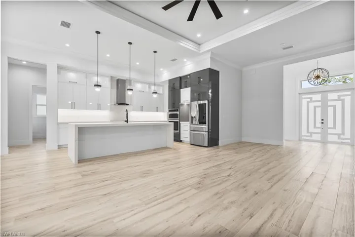 Kitchen with wall chimney range hood, light countertops, modern cabinets, light wood-style floors, and appliances with stainless steel finishes