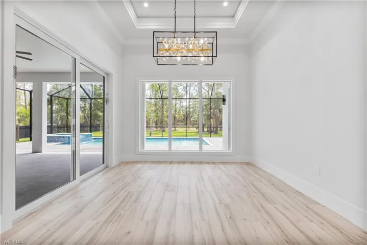 Unfurnished dining area featuring a raised ceiling, wood finished floors, ornamental molding, a chandelier, and baseboards