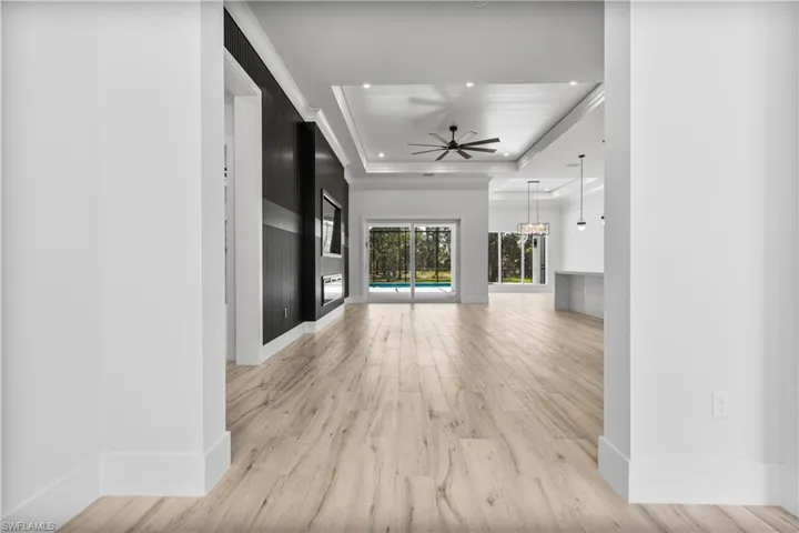 Unfurnished living room featuring a tray ceiling, light wood finished floors, baseboards, a chandelier, and recessed lighting