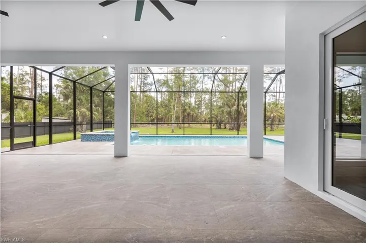 View of swimming pool featuring ceiling fan, a patio area, a lanai, a pool with connected hot tub, and a lawn