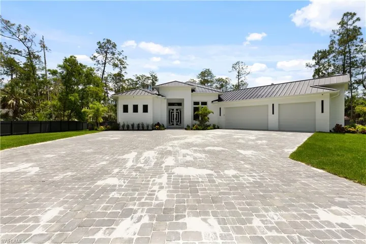 Modern farmhouse style home featuring a standing seam roof, decorative driveway, an attached garage, and metal roof