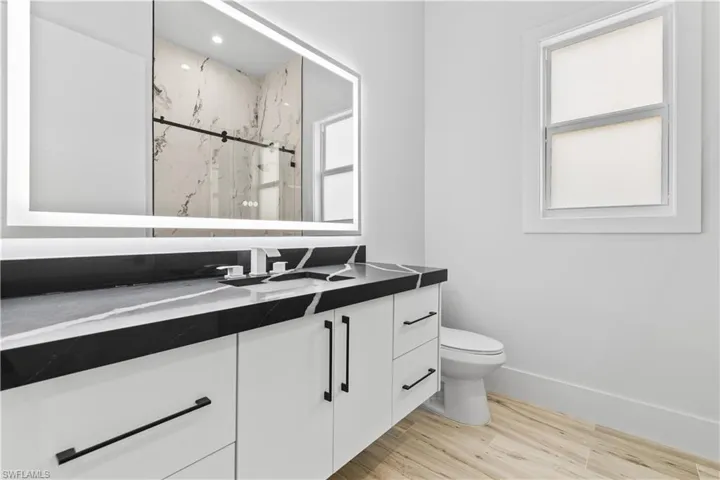 Bathroom with vanity, a marble finish shower, wood finished floors, toilet, and baseboards