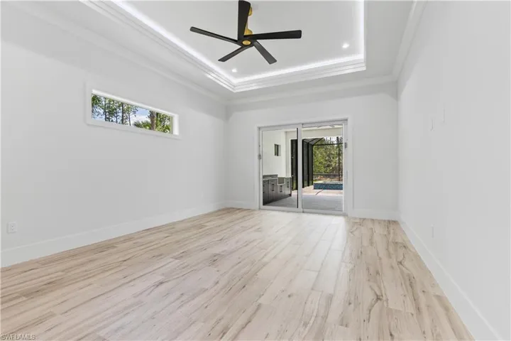 Empty room featuring a tray ceiling, light wood-style flooring, crown molding, a ceiling fan, and baseboards