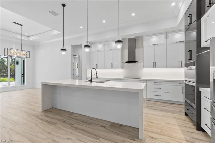 Kitchen featuring wall chimney range hood, modern cabinets, crown molding, a sink, and a raised ceiling