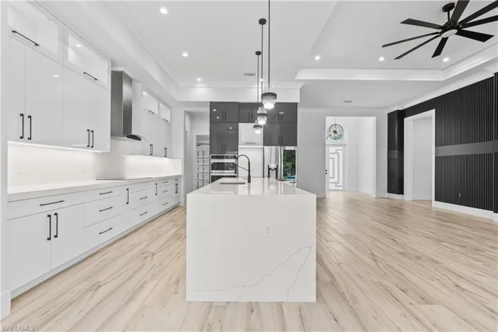 Kitchen with modern cabinets, wall chimney range hood, a ceiling fan, a raised ceiling, and crown molding