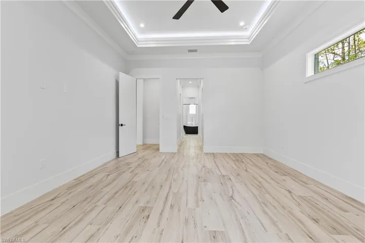 Spare room with a ceiling fan, a tray ceiling, ornamental molding, wood finished floors, and baseboards