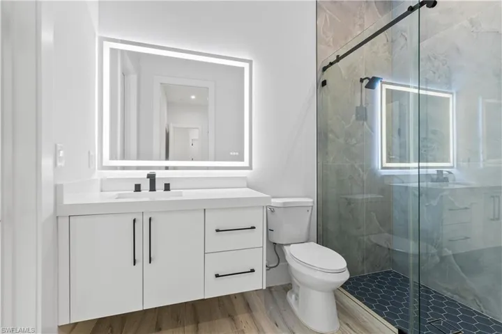 Full bath with toilet, vanity, a marble finish shower, and wood finished floors