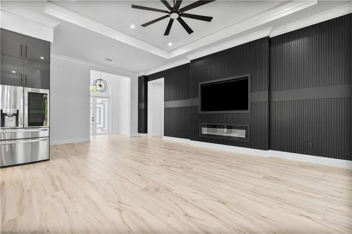 Unfurnished living room with a ceiling fan, ornamental molding, light wood-style floors, a tray ceiling, and a glass covered fireplace