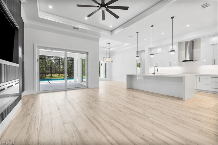 Unfurnished living room with a raised ceiling, light wood finished floors, a ceiling fan, recessed lighting, and a sink