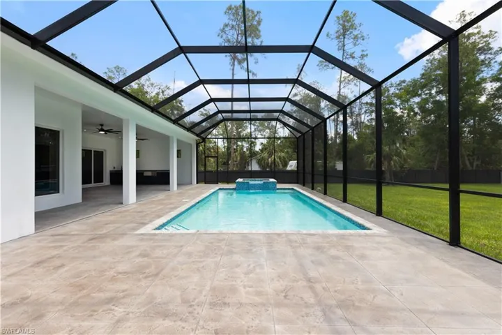 View of pool with ceiling fan, a yard, a patio area, a pool with connected hot tub, and glass enclosure