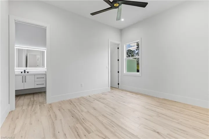 Unfurnished bedroom featuring light wood-type flooring, a sink, baseboards, ensuite bathroom, and a ceiling fan