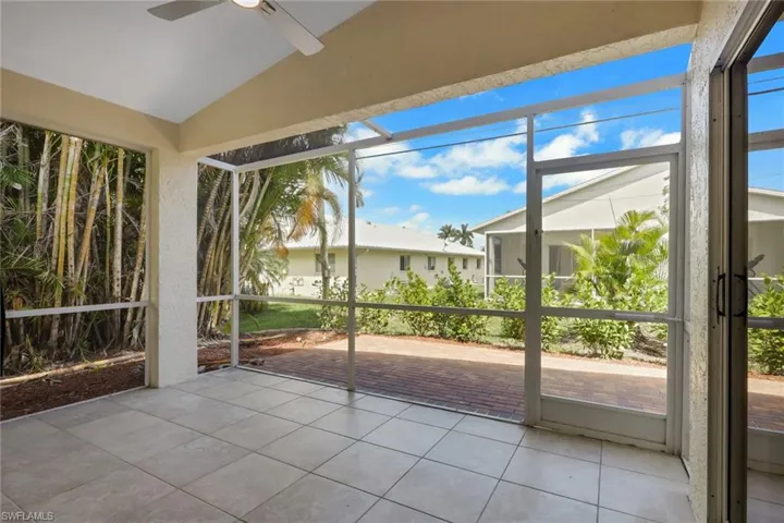 Screened lanai featuring tile flooring, a ceiling fan, and direct access to a brick paver patio and mature tropical landscaping