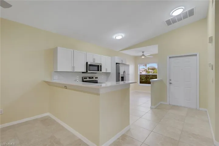 Open concept living space featuring a kitchen with white cabinetry, stainless steel appliances, and a breakfast bar