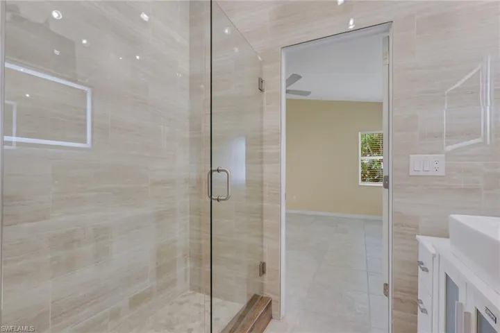 Glass-enclosed shower with stone-look tile surround and built-in bench