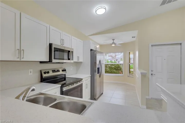 Modern kitchen featuring white shaker cabinetry, stainless steel appliances, a dual basin sink, and light-toned countertops