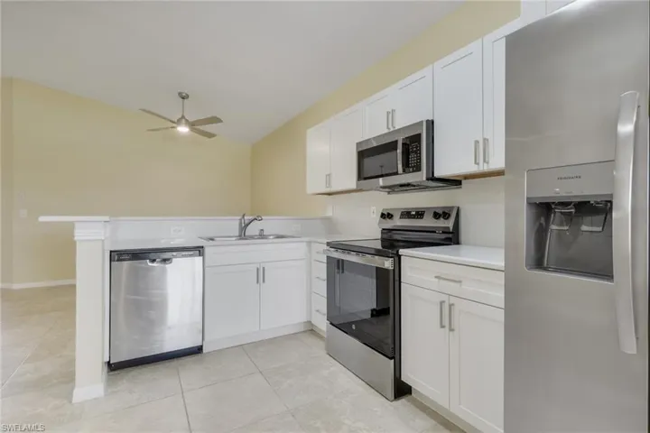 Kitchen featuring white cabinetry, stainless steel appliances, solid surface countertops, a bar height counter, and tile flooring