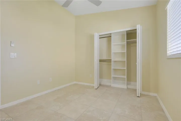 Bright interior room featuring vaulted ceilings, tile flooring, a ceiling fan, and a built-in closet system with shelving and hanging rods