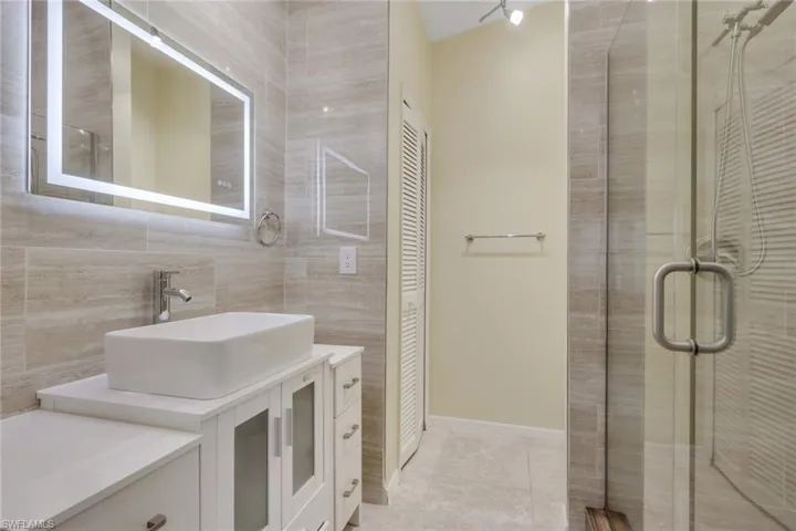 Contemporary vanity with a vessel sink, an illuminated mirror, and a glass-enclosed shower with tiled walls