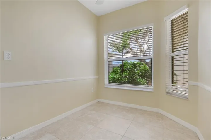 Corner room featuring two windows with horizontal blinds, tile flooring, and light-toned walls with chair rail molding