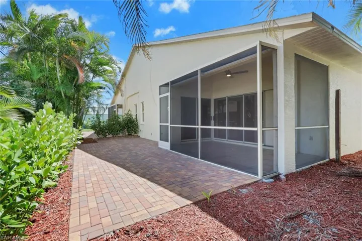 Exterior featuring a screened patio with a ceiling fan, brick paver patio, mature tropical landscaping, and decorative red mulch