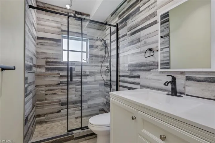 Bathroom featuring a glass-enclosed shower with black trim, a vanity with a white countertop and built-in sink, and a wall-mounted mirror