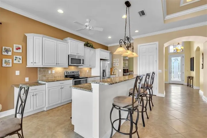 Kitchen with dark stone countertops, a kitchen breakfast bar, white cabinets, stainless steel appliances, and ornamental molding