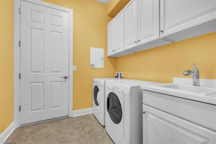 Laundry area with cabinet space, light tile patterned floors, and washer and clothes dryer