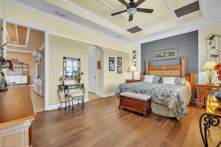 Bedroom with arched walkways, wood finished floors, a ceiling fan, crown molding, and coffered ceiling