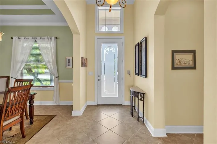 Entryway with arched walkways, crown molding, suspended lighting, and light tile patterned floors