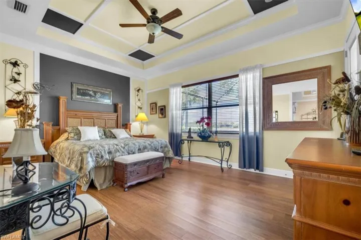 Bedroom featuring wood finished floors, a ceiling fan, coffered ceiling, and ornamental molding