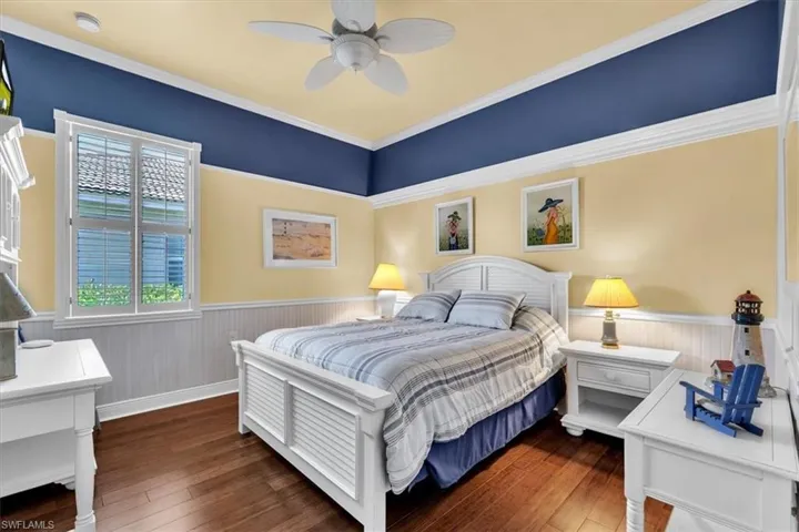 Bedroom featuring wainscoting, dark wood-style flooring, ceiling fan, and crown molding