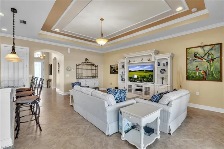 Living area featuring crown molding, arched walkways, a tray ceiling, recessed lighting, and light tile patterned flooring