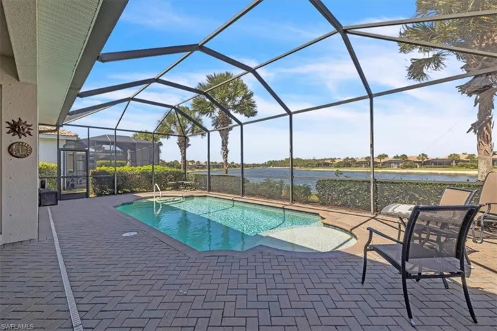 Outdoor pool with a sunroom, a patio area, glass enclosure, and a water view