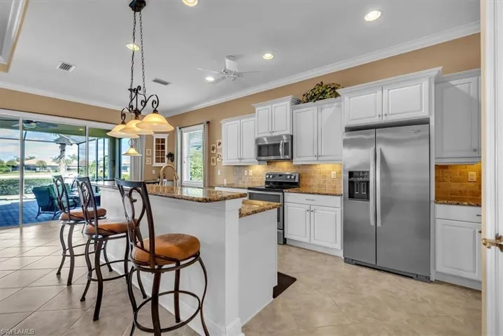 Kitchen featuring stainless steel appliances, dark stone countertops, white cabinets, ceiling fan, and a breakfast bar