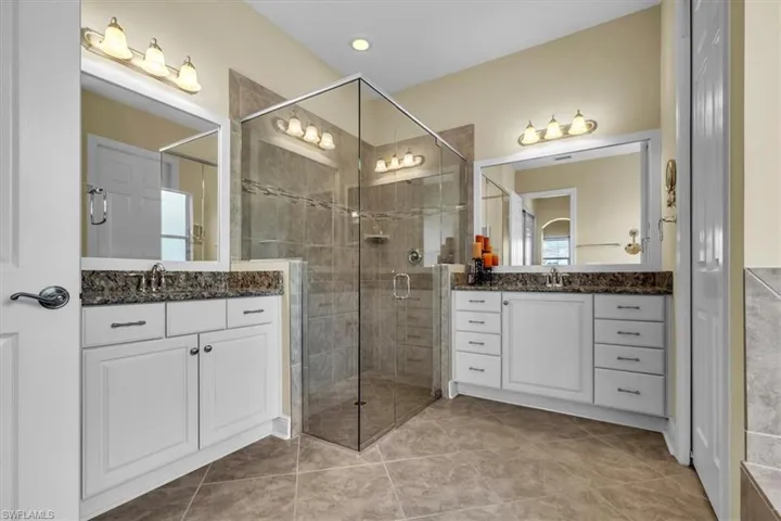 Bathroom with two vanities, a shower stall, and light tile patterned floors