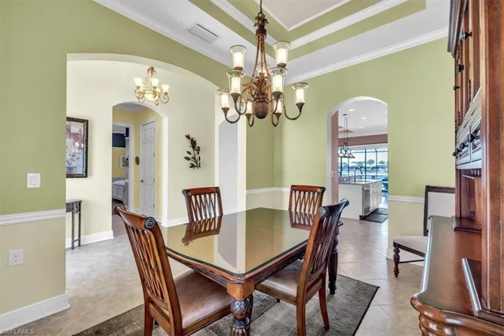 Dining room with a chandelier, light tile patterned floors, a raised ceiling, ornamental molding, and arched walkways