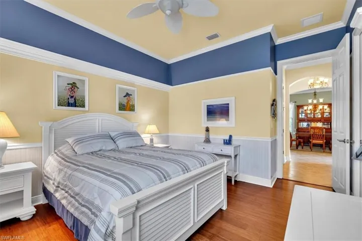Bedroom featuring a wainscoted wall, wood finished floors, suspended lighting, a ceiling fan, and crown molding