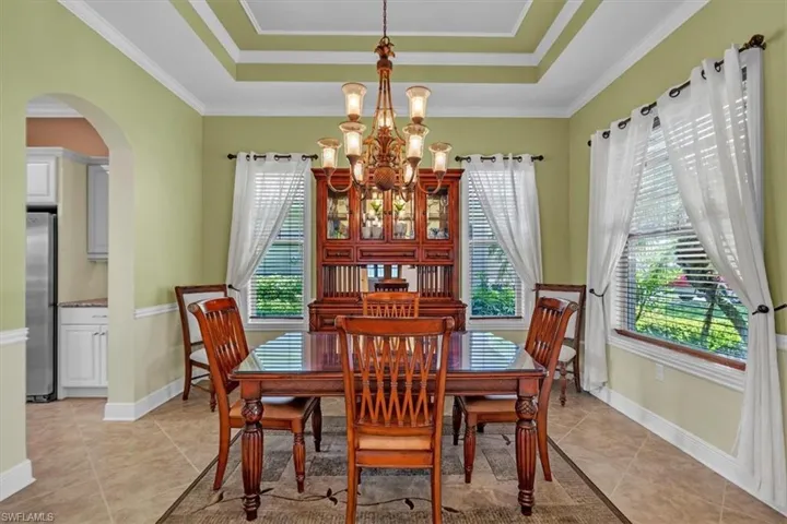 Dining area featuring arched walkways, suspended lighting, crown molding, a tray ceiling, and light tile patterned flooring