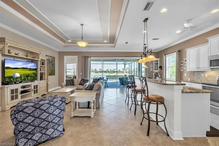 Living room featuring a ceiling fan, crown molding, a raised ceiling, and light tile patterned flooring