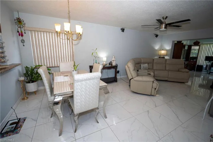 Dining space featuring a chandelier, light marble finish floors, ceiling fan, and a textured ceiling