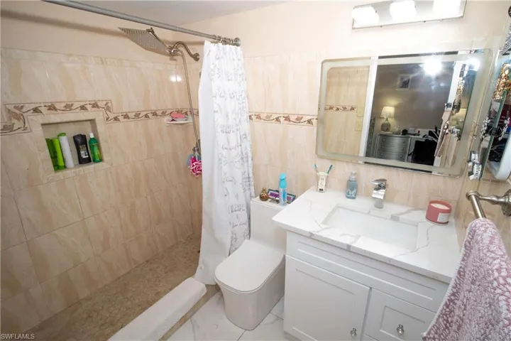 Bathroom with a tile shower, vanity, tile walls, and decorative backsplash